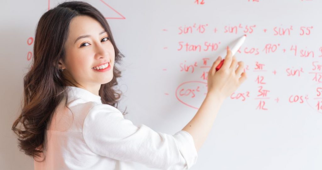 Female Math tutor writing Math Formulas on the whiteboard at tuition centre