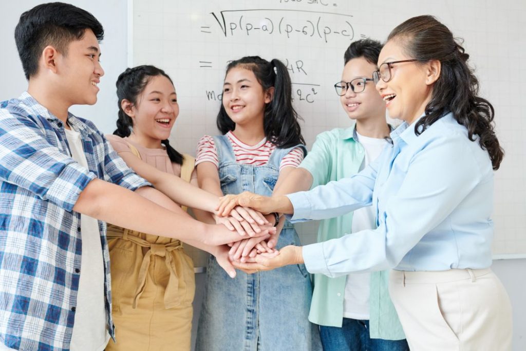 Secondary School Students stacking hands with their mathematics tutor